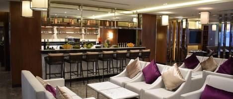Un moderno vestíbulo de hotel con sofás blancos, una zona de bar y una cocina al fondo.