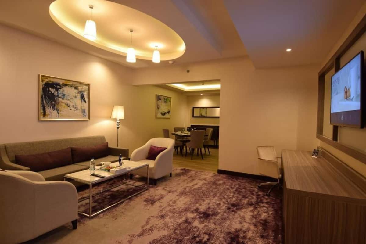 Een hotelkamer met een bank, fauteuils, een salontafel, een televisie en een bureau.