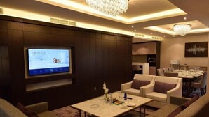 Une chambre d’hôtel moderne dotée d’un grand écran diffusant une présentation, de sièges confortables et d’un espace repas.