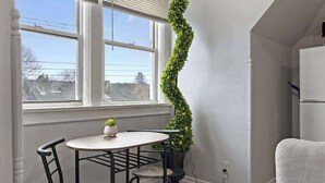 Un petit coin repas avec une table ronde et deux chaises, une plante en pot et une vue par la fenêtre.