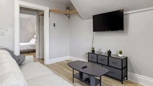 Un salon moderne comprenant un canapé, une petite table, un téléviseur fixé au mur et un meuble contenant des objets décoratifs.
