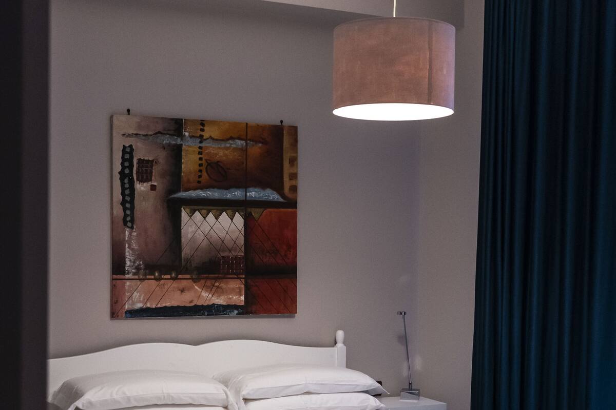 Ein modernes Schlafzimmer mit einem weißen Bett, einer Hängelampe und einem Gemälde an der Wand.