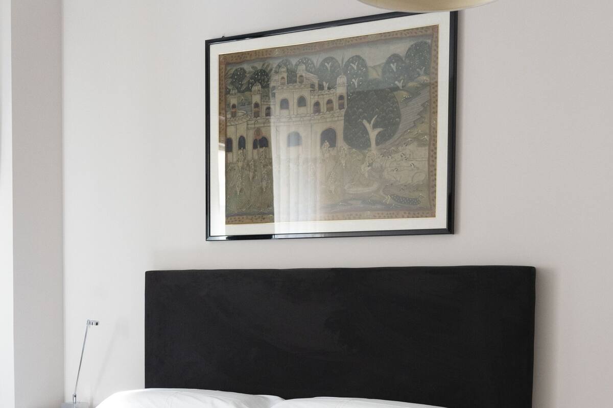 Ein modernes Schlafzimmer mit einem großen Bett, einem Nachttisch, einem Beistelltisch und einem gerahmten Kunstwerk an der Wand.