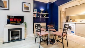Una sala de estar moderna con chimenea, un televisor que muestra 'NETFLIX' y un comedor con sillas y una mesa.