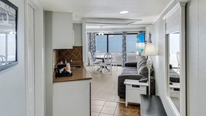 A compact living space with a kitchenette, a dining area with a table and chairs, a sofa, and a view of the ocean through large windows. - Vacation Time Oceanfront Deluxe Queen Room 4th Flr (Pawleys Island)