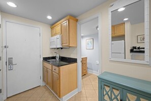 Una cucina compatta con mobili in legno, un piano di lavoro nero e un forno a microonde bianco.