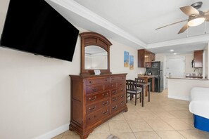 A room with a wooden dresser, a flat-screen TV, a ceiling fan, a dining area with chairs, and a kitchen area. - Dunes King Room Oceanfront Views (Pawleys Island)