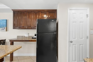Una cocina con armarios de madera, un refrigerador negro, encimera de granito y una puerta blanca.