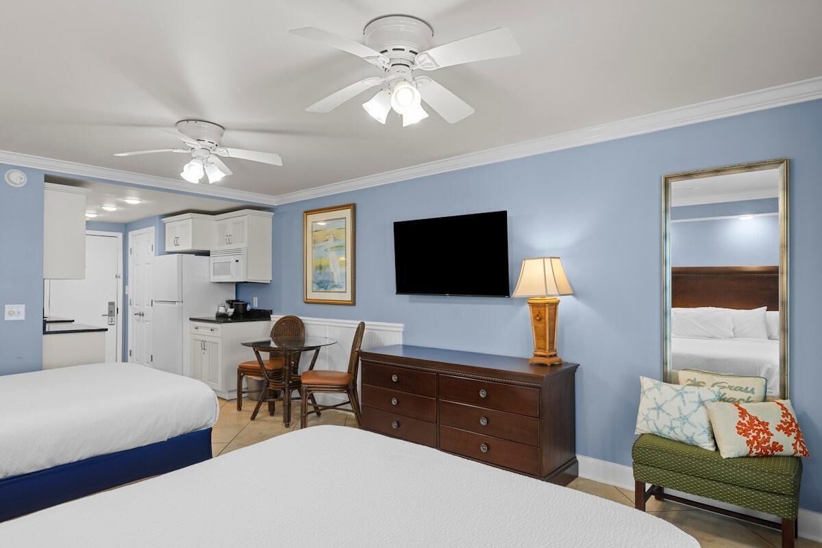 Une chambre d’hôtel équipée d’un lit, d’un bureau, d’une chaise, d’une commode, d’une télévision et d’un ventilateur de plafond.