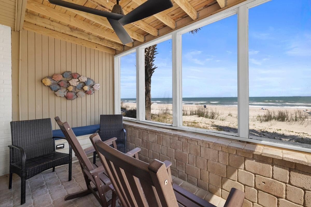 A covered outdoor seating area with wicker chairs and a table, overlooking a beach.