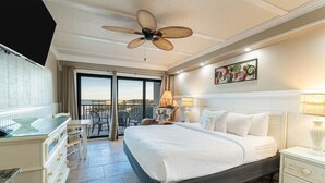 Camera d'albergo con un letto grande, una ventola a soffitto, un balcone con tavolo e sedie e vista sul mare.