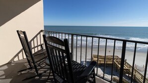 A balcony with a view of the beach, featuring a wooden bench and a chair.