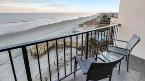 A balcony with a view of the beach, a glass table, and wicker chairs. - Beachy 5th Floor Oceanfront Room (Pawleys Island)