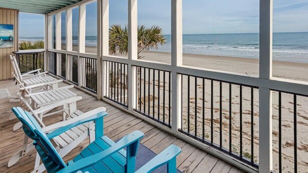 A covered deck with wooden chairs and a view of the beach.