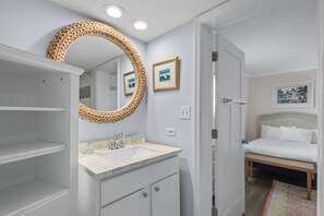 Une salle de bain avec un grand miroir, un lavabo et une porte donnant sur une chambre.
