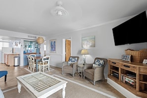 A living room with a dining area, a television, wicker furniture, and a bookshelf. - Gorgeous Oceanfront 2 Bedroom Villa (Pawleys Island)