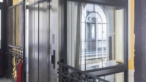 Ein Aufzug mit Glastrennwand, Metallgeländern und einem Feuerlöscher an der Wand.