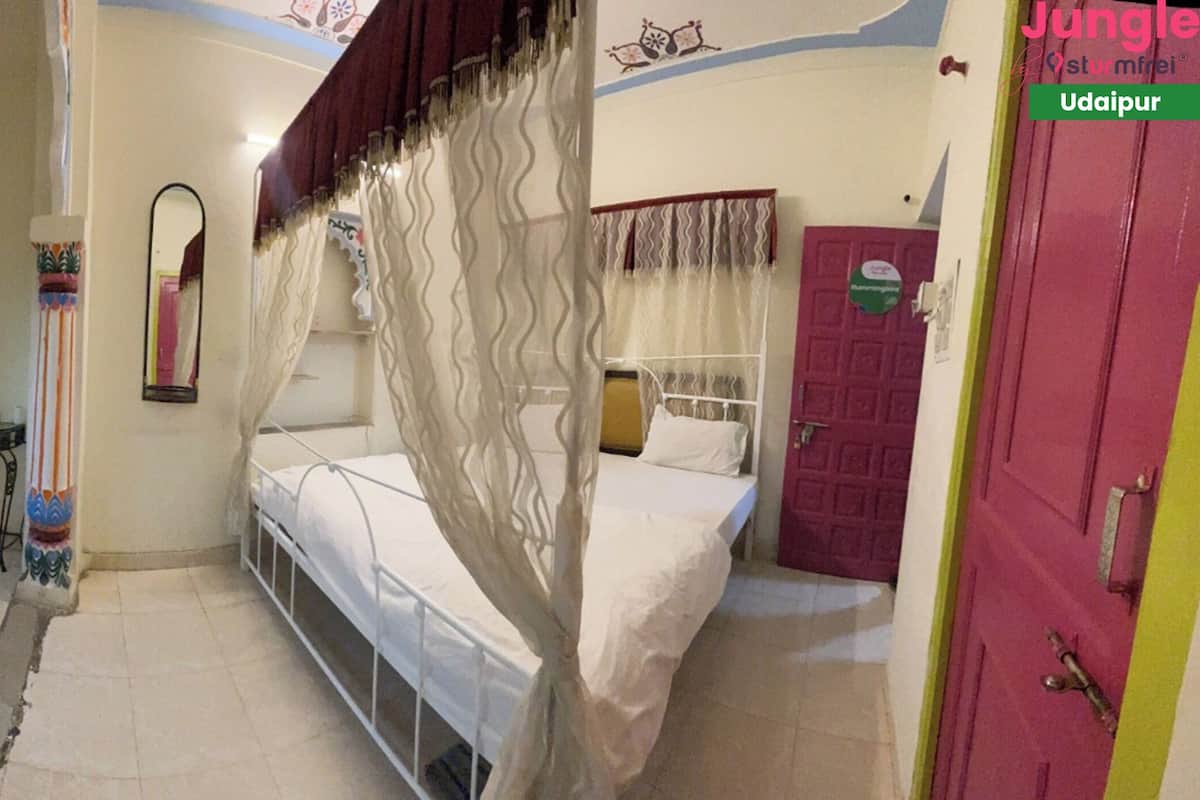 Una habitación con cama, una silla, una mesa y ventana con cortinas.