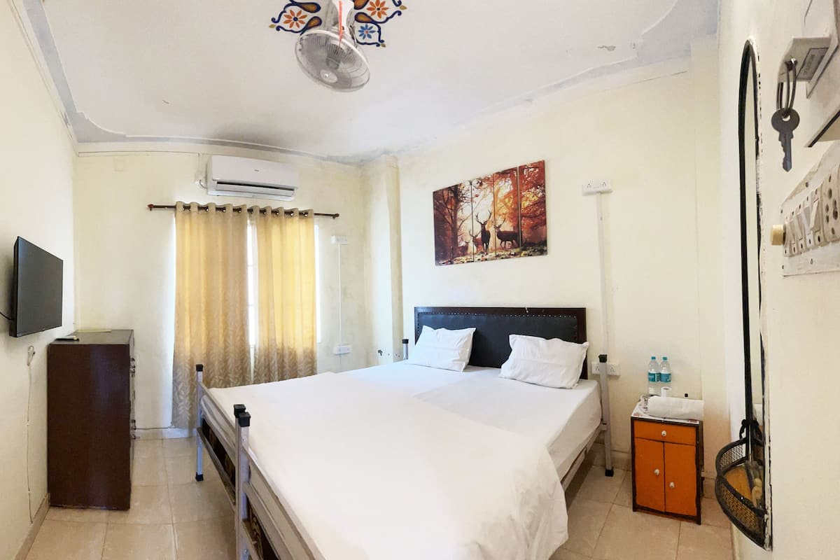 Habitación de hotel con una cama grande, un televisor, un equipo de aire acondicionado, un cuadro, un mueble pequeño y un atarraque para llaves en la pared.