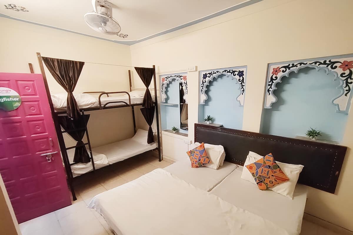 Una habitación con literas, una cama grande con almohadas estampadas y espejos decorativos en la pared.
