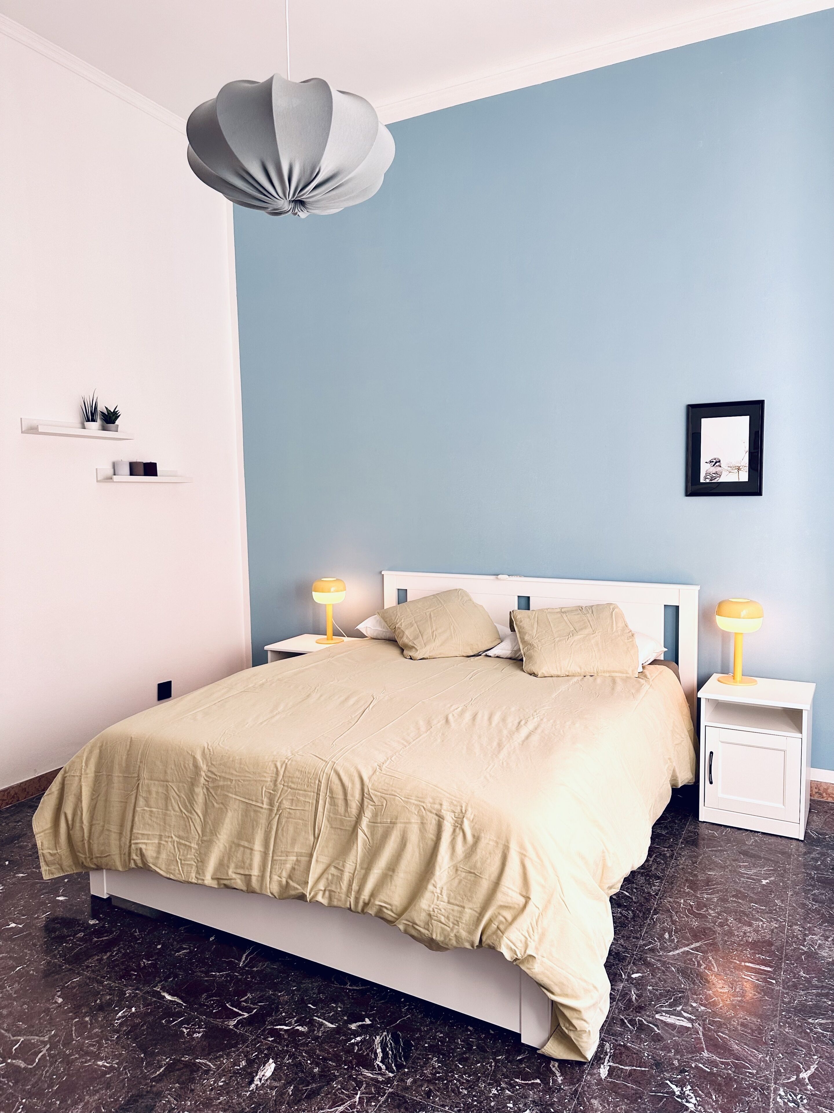 Un dormitorio moderno con cama, mesitas de noche, lámpara colgante y un cuadro enmarcado en la pared.
