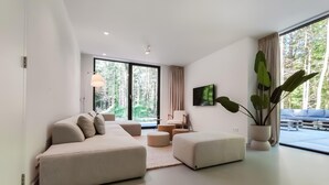 Un salon moderne avec un canapé, un pouf et une grande plante en pot.