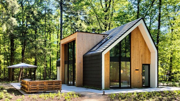 Une cabane en bois moderne, dotée de grandes fenêtres, d’un toit en pente et d’un banc à l’extérieur.