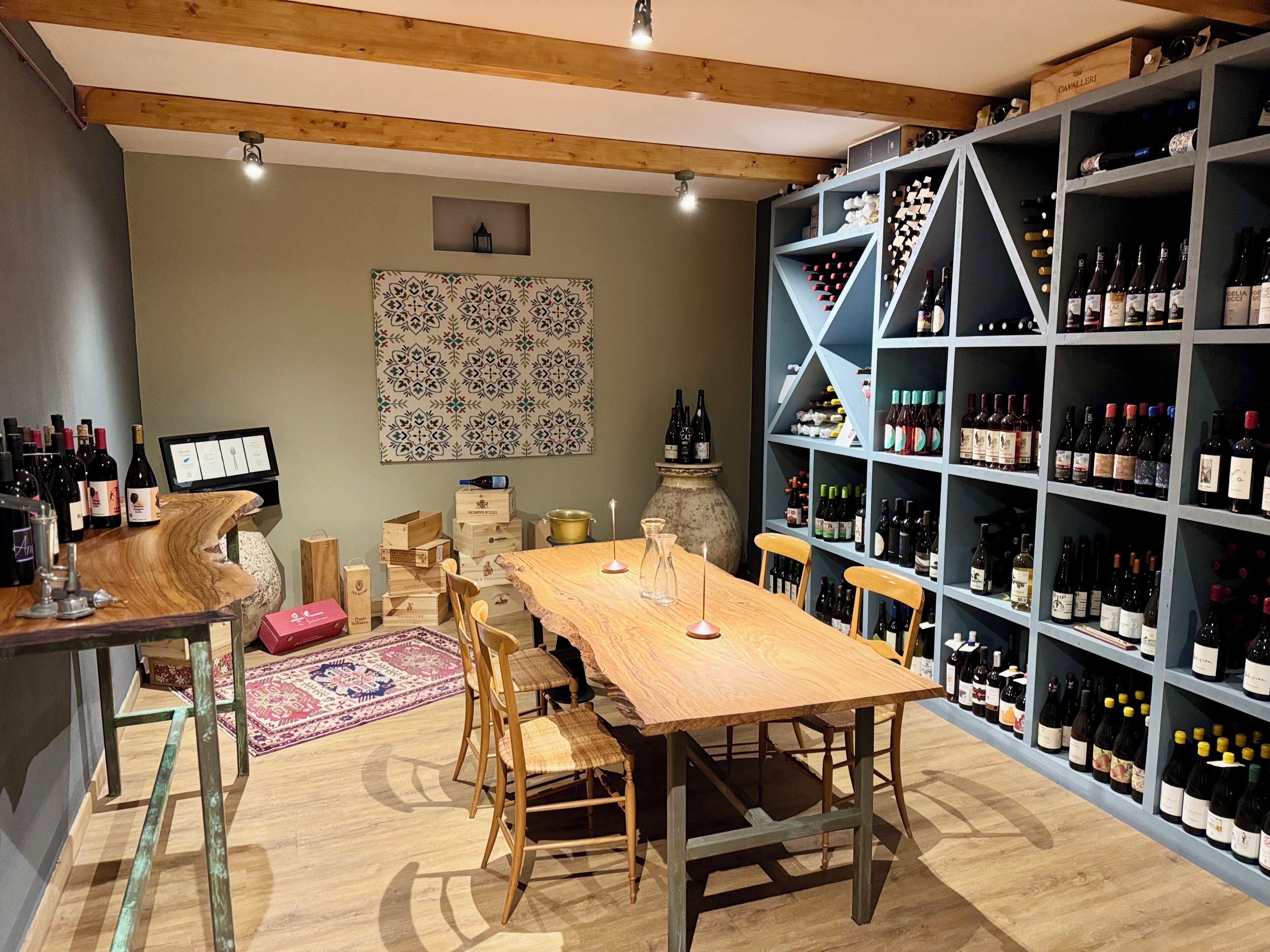 Una bodega con una mesa y sillas de madera, rodeada de estantes llenos de botellas de vino.