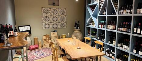 Una bodega con una mesa y sillas de madera, rodeada de estantes llenos de botellas de vino.