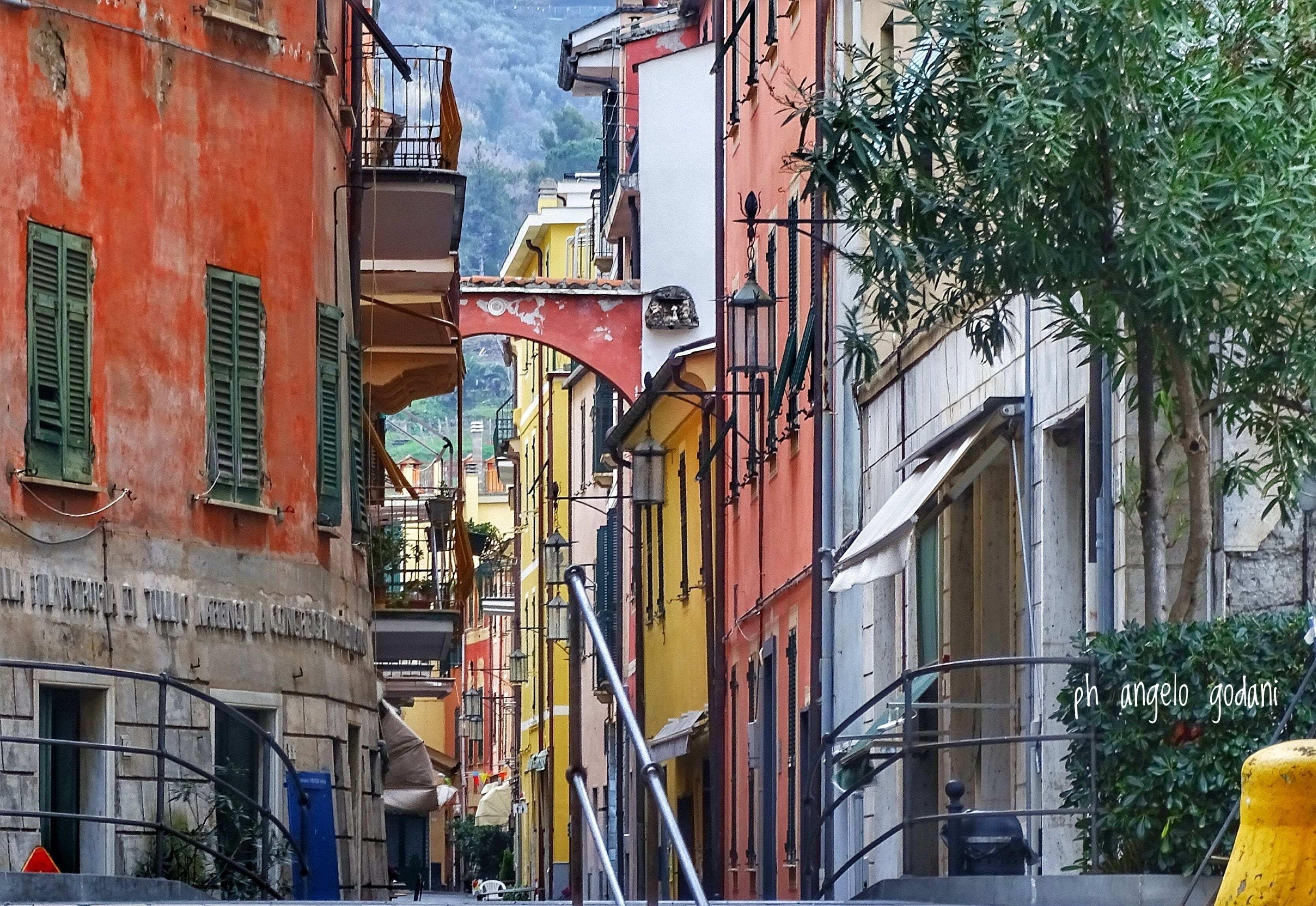 A narrow street with colorful buildings, balconies, and a mountain in the background.
