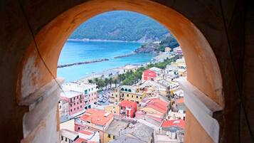 A coastal town viewed through an archway, featuring colorful buildings, a beach, and a mountainous backdrop.