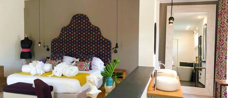 A modern hotel room with a large bed, a wooden bedside table, a mirror, and a bathroom visible through an open door.