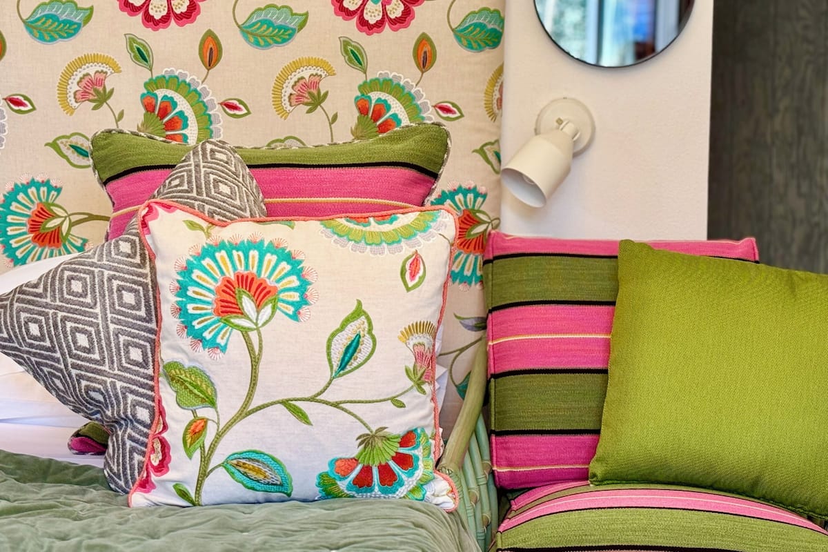 Una cama con almohadones coloridos y un papel tapiz estampado con flores.