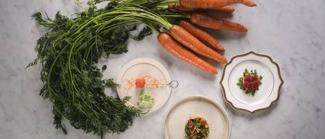 A top-down view of a kitchen counter with fresh carrots, parsley, and two plates with food.