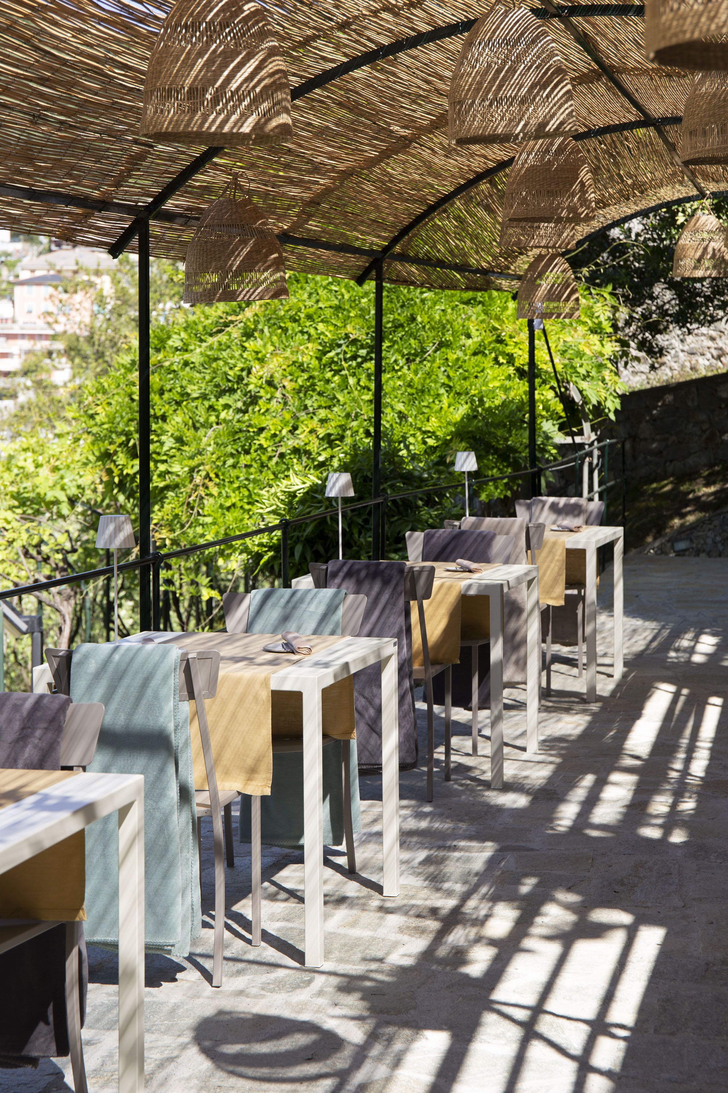 Un espace extérieur aménagé avec des tables et des chaises, protégé par une tonnelle en osier et entouré de verdure.