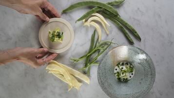 Vista cenital de una cocina con encimera de mármol, un plato de cerámica con guarnición verde y diversas verduras como judías verdes y calabacín.