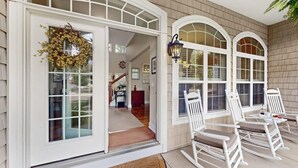A house with a front porch featuring white rocking chairs and a large window with a wreath.