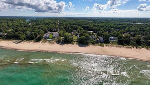 An aerial view of a coastal area with a beach, dense greenery, and scattered houses.