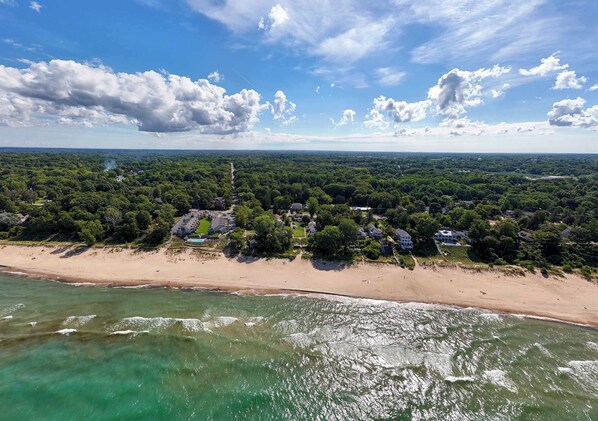 An aerial view of a coastal area with a beach, dense greenery, and scattered houses.