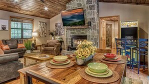 A cozy living room with a stone fireplace, a television mounted on the wall, and a Pac-Man arcade machine.