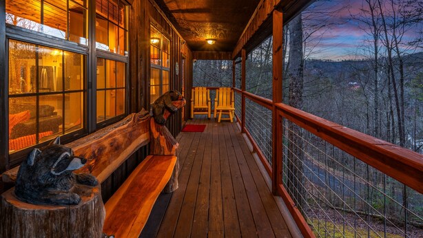 A wooden deck with a bench and chairs, large windows, and a view of a forested landscape.