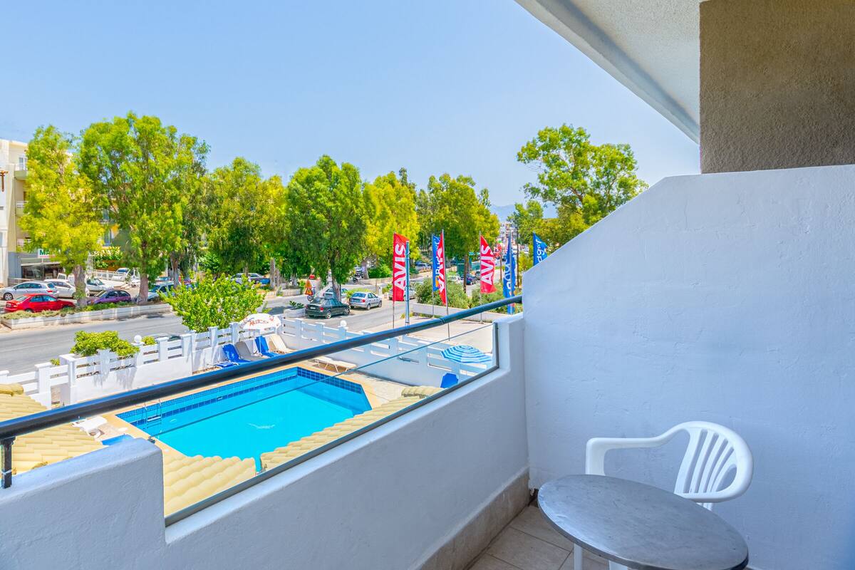 A balcony with a view of a swimming pool, a white chair, and a railing.