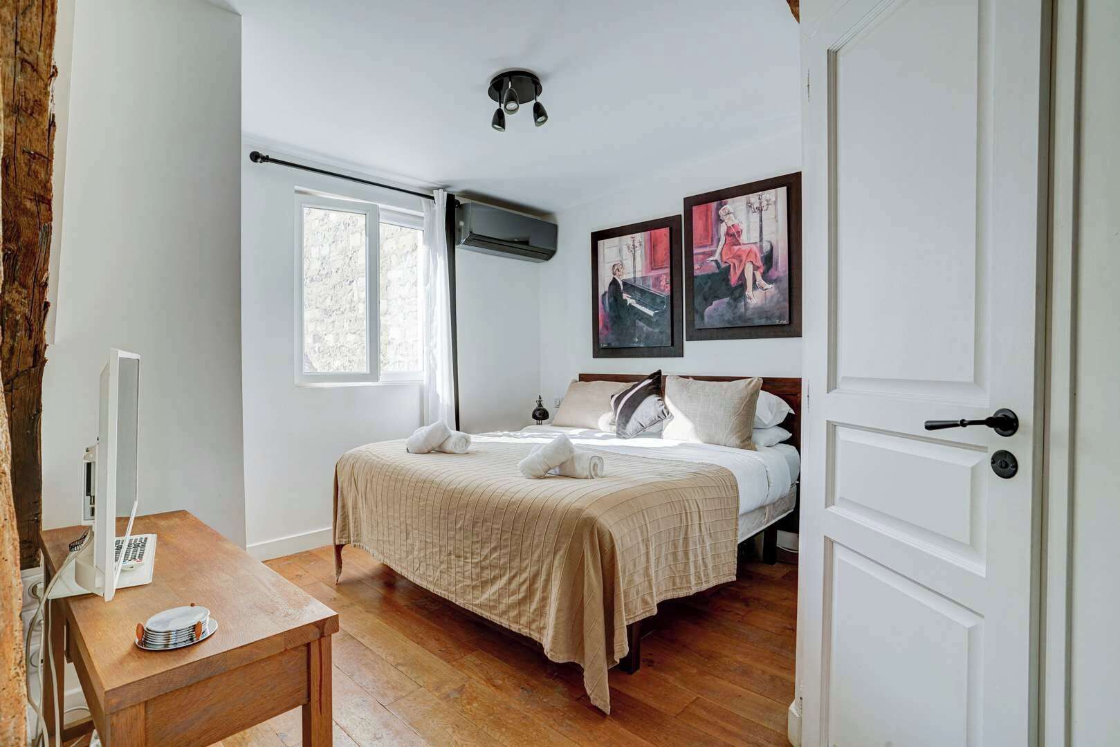 Ein Schlafzimmer mit einem Bett, einem Schreibtisch, einem Fenster und zwei Bildern an der Wand.