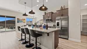 A modern kitchen with a central island, bar stools, stainless steel appliances, and pendant lighting.