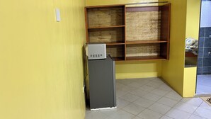 A corner room with a wooden shelf unit against the wall, a small gray cabinet, and a tiled floor. - 020-22Airbnbs (Thika)