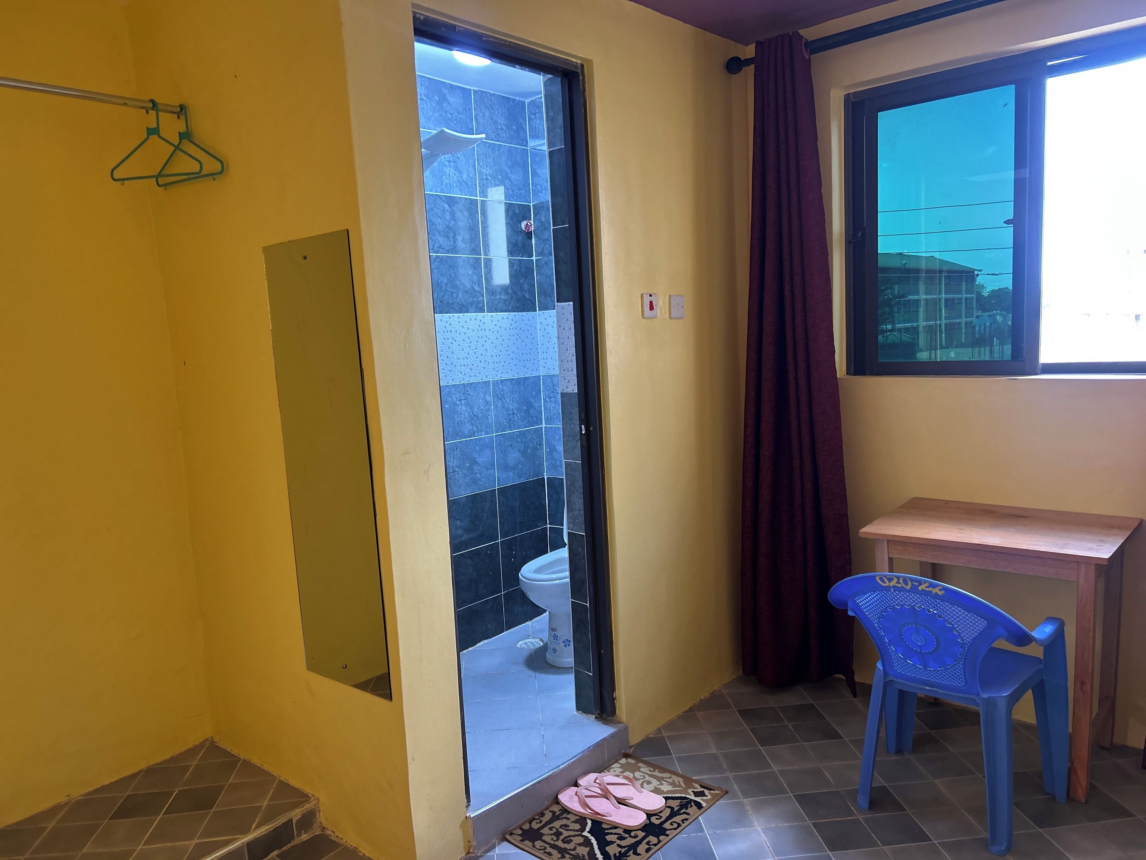 Une petite salle de bain avec des toilettes, une douche, une chaise en plastique bleue et une table en bois.