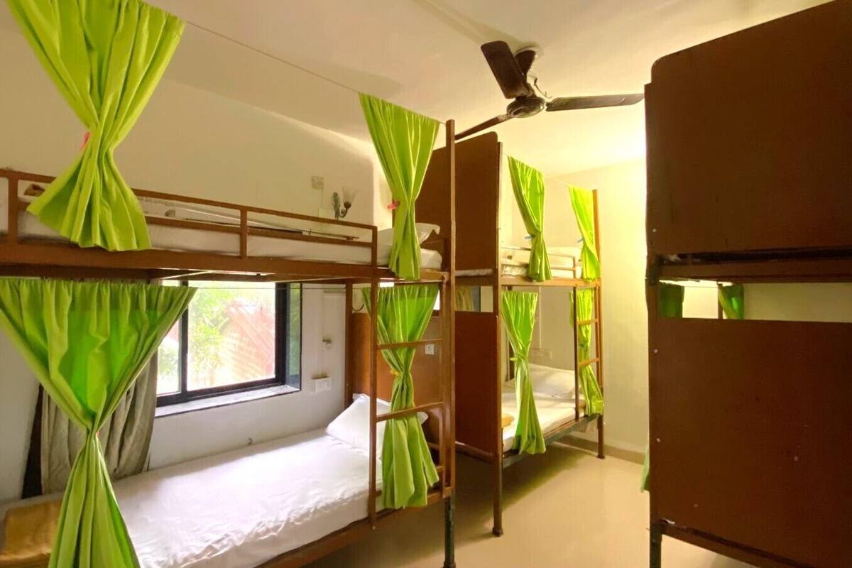 A dormitory room with bunk beds, green curtains, a ceiling fan, and a window.