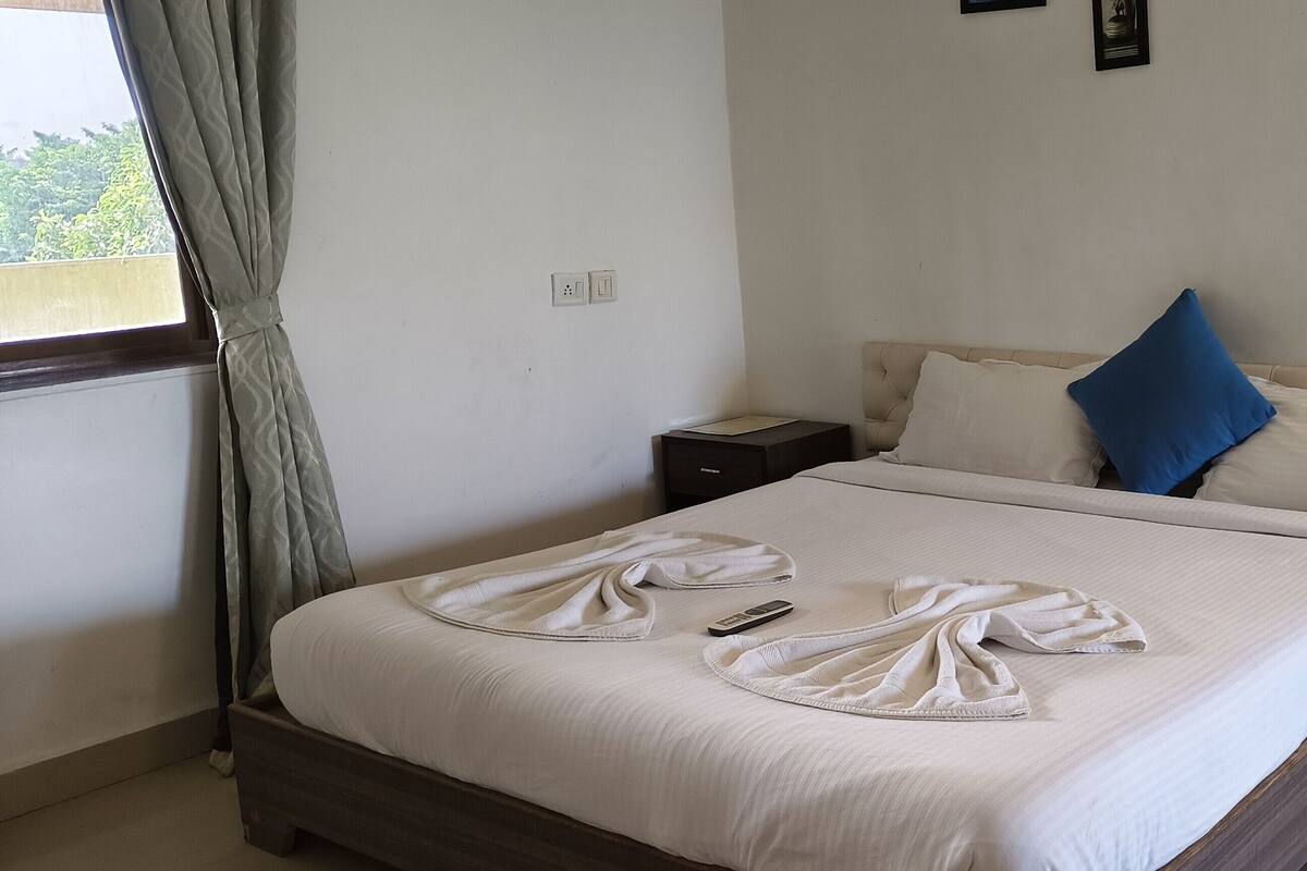 A neatly made bed with towels and a remote control, a bedside table, and a window with curtains.