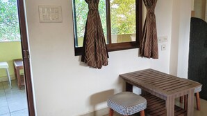 A small kitchenette with a microwave, a sink, and wooden cabinets. There is a window with curtains, a table with a checkered stool, and a chair. - Jungle by sturmfrei Vagator (Vagator)