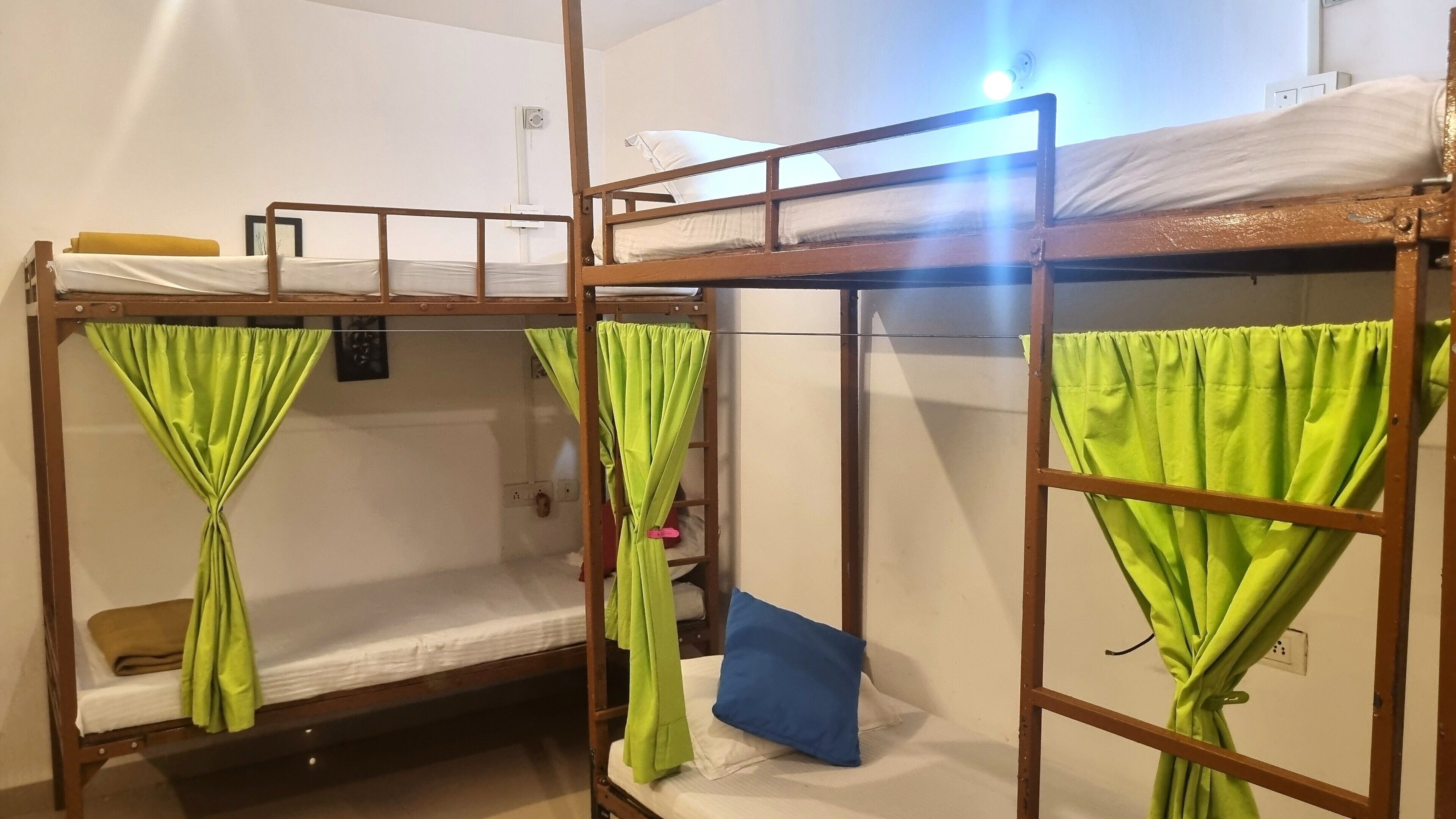 A dormitory room with bunk beds, green curtains, and a blue pillow.